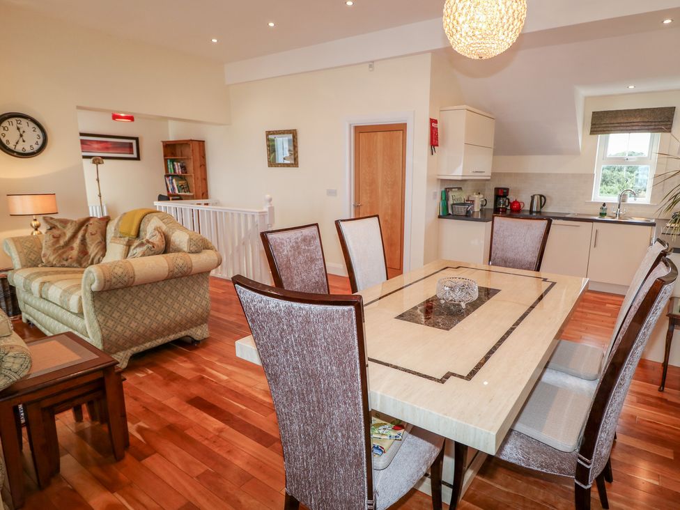 A dining table with six chairs next to a kitchen and a seating area with sofas in an open living space at Seaview in Castlerock