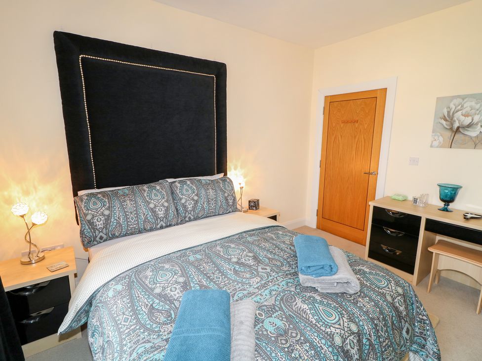 A bedroom with a bed with patterned bedding bedside tables with lamps a wooden door and a dresser with a blue vase at Seaview in Castlerock
