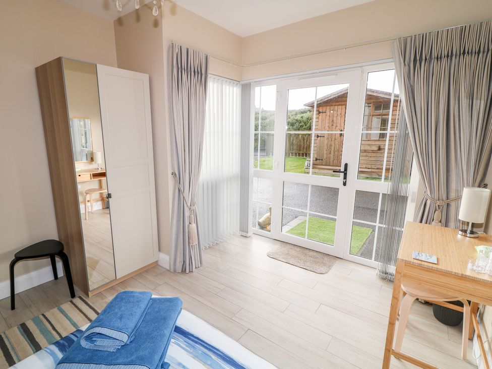 A bedroom with a wardrobe mirror desk and glass doors leading to a garden at Seaview in Castlerock