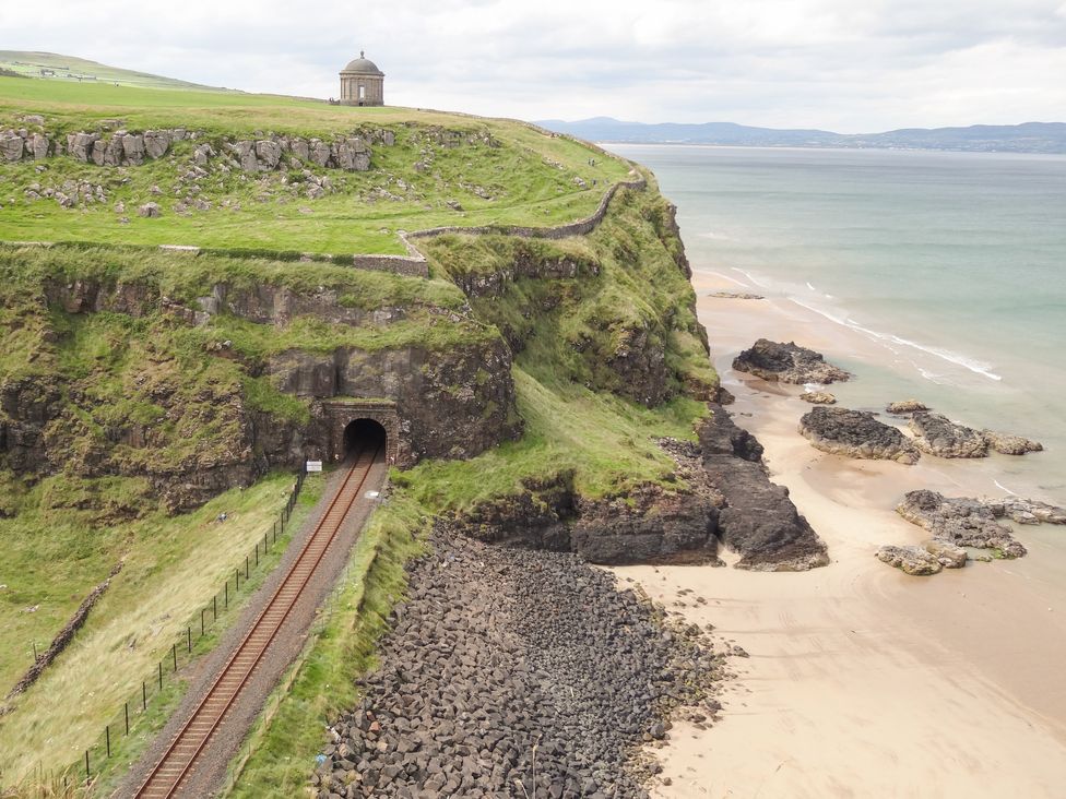 Railway track entering a tunnel on a grassy cliff beside a rocky beach and sea at Seaview in Castlerock