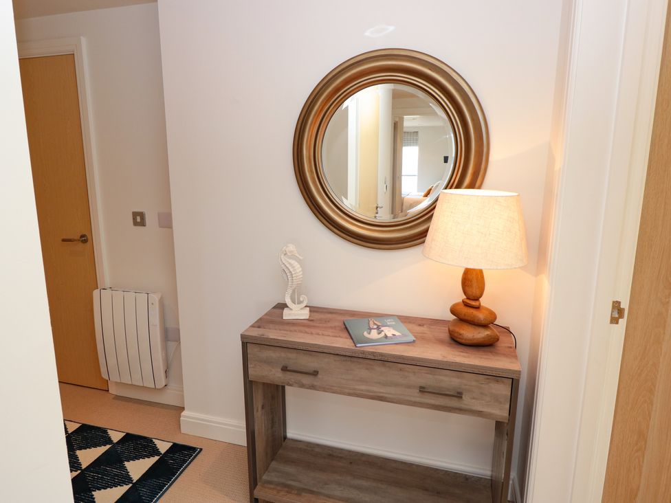 A hallway with a wooden console table with a table lamp a seahorse ornament and a book under a round mirror at 7 Ocean's Edge in Thurlestone