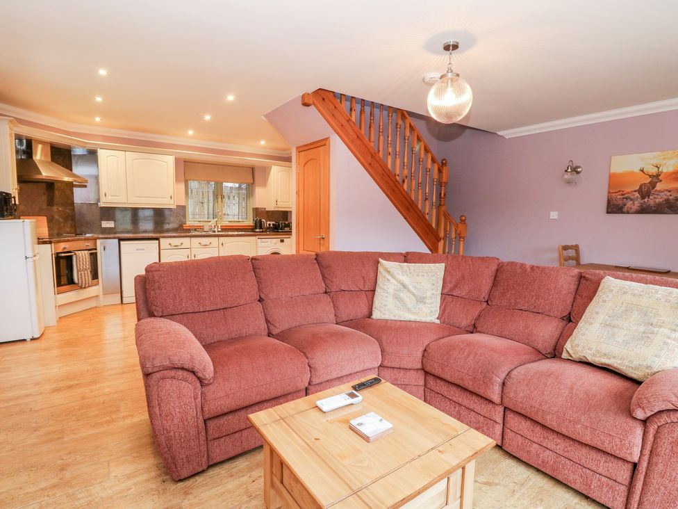 An open living room and kitchen area with a red sectional sofa and wooden staircase at Little Tigh Clovelly in Spean Bridge