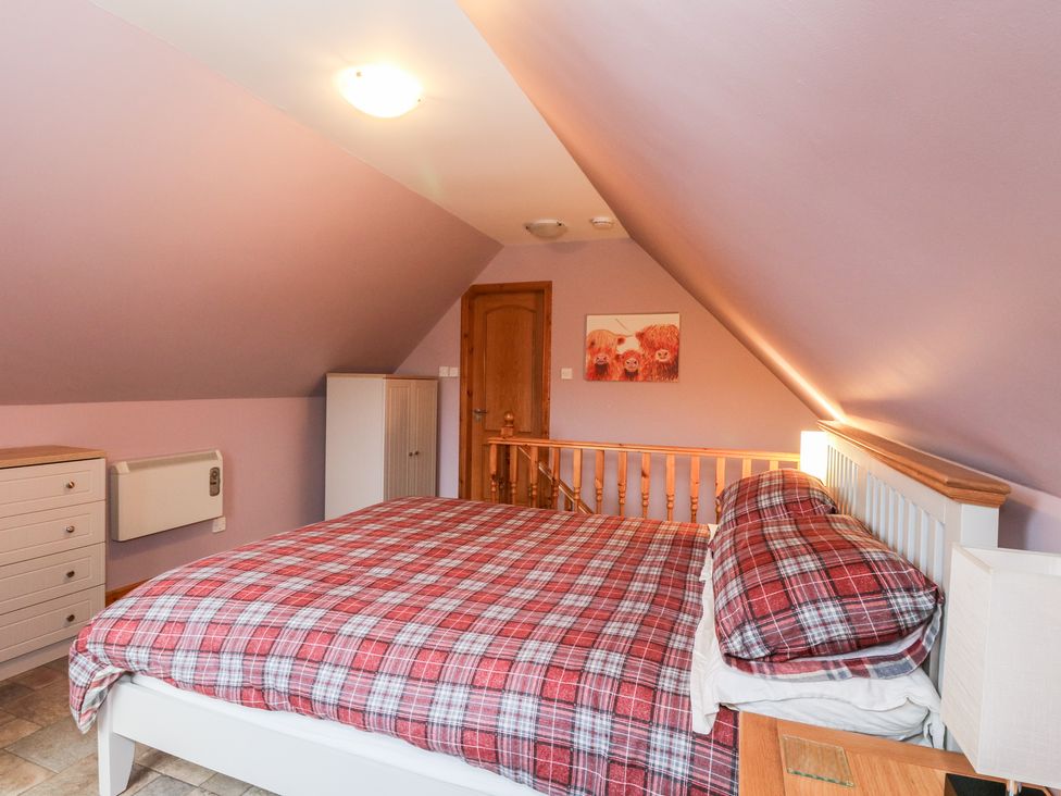 A bedroom with a bed with red plaid bedding a wooden door a white dresser a small cabinet and a painting of three cows on the wall at Little Tigh Clovelly in Spean Bridge