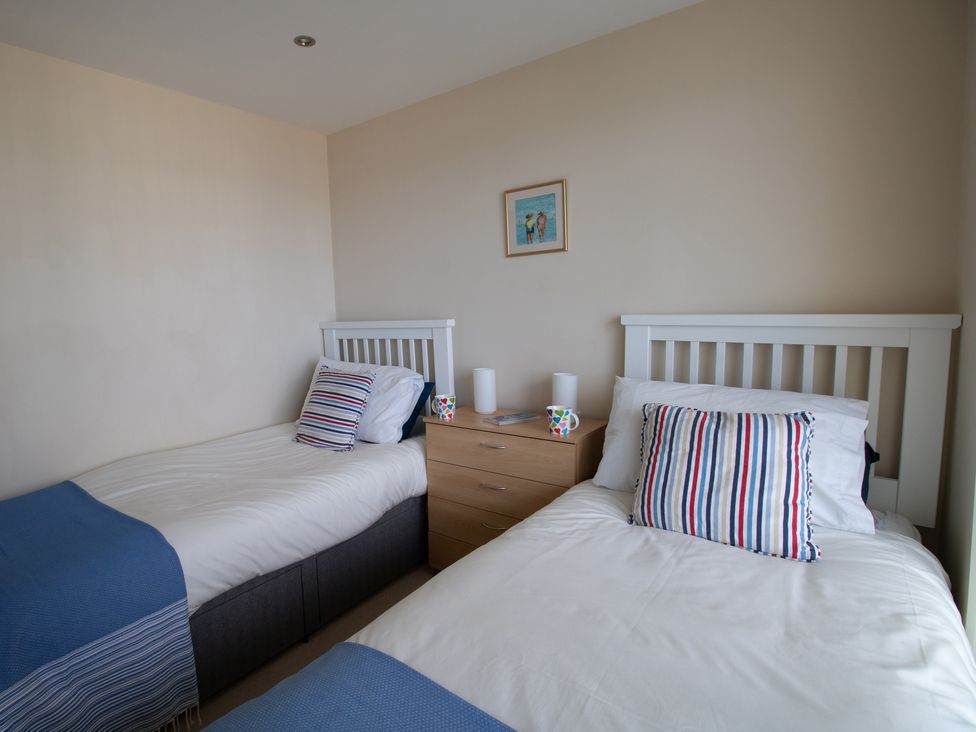 A bedroom with two single beds pillows striped cushions a wooden nightstand with mugs and lamps a framed picture on the wall at Panoramic View in Castletown Portland
