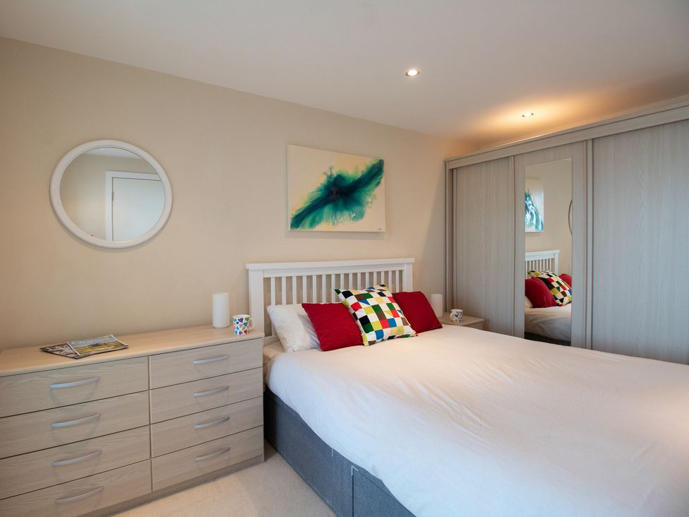 A bedroom with a bed with pillows a dresser with mugs a round mirror and sliding wardrobe doors at Panoramic View in Castletown Portland