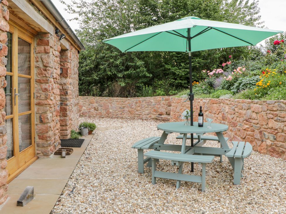 A patio area with a round picnic table and umbrella surrounded by stone walls and plants at The Old Haybarn in Ipplepen