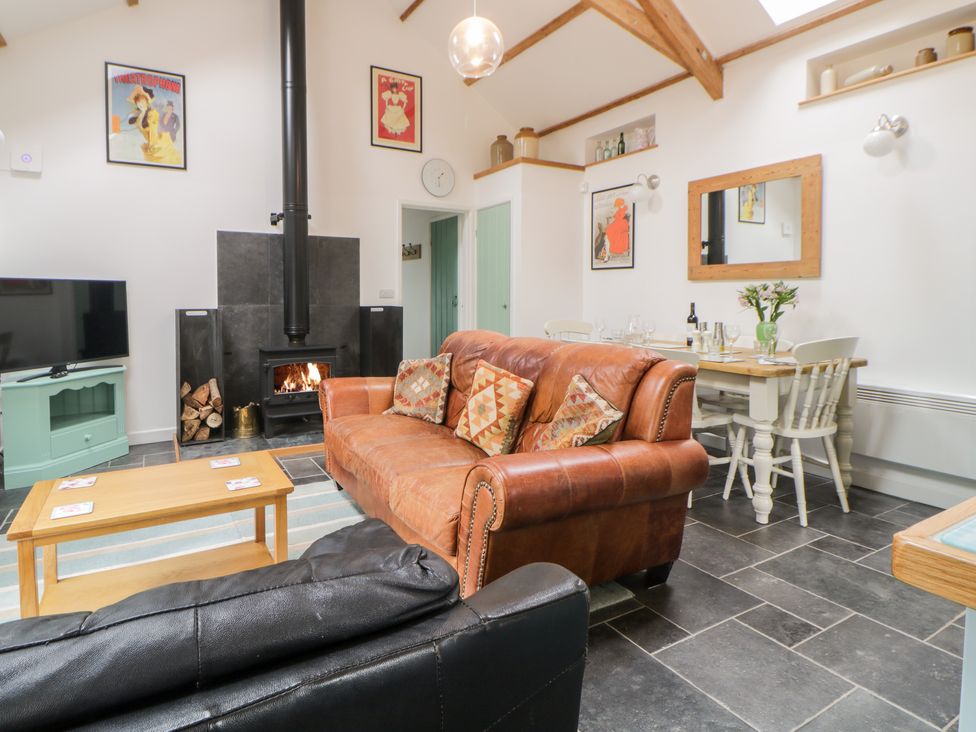 A living room with a leather sofa a wood stove and a dining table at The Old Haybarn in Ipplepen