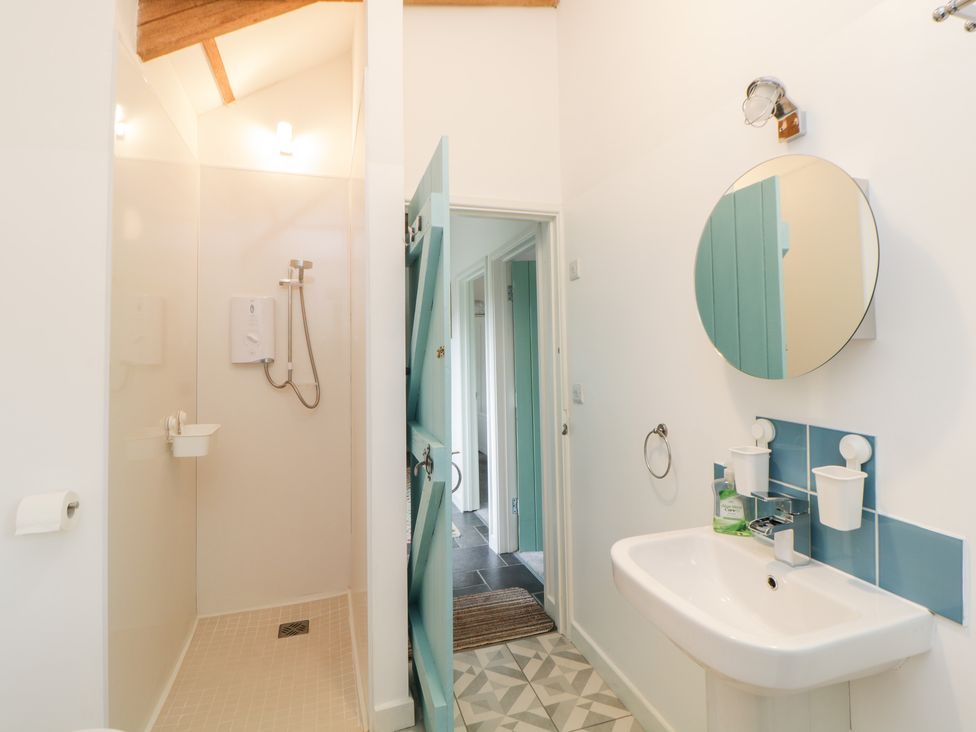 A bathroom with a shower area a sink a round mirror and a partially open door at The Old Haybarn in Ipplepen