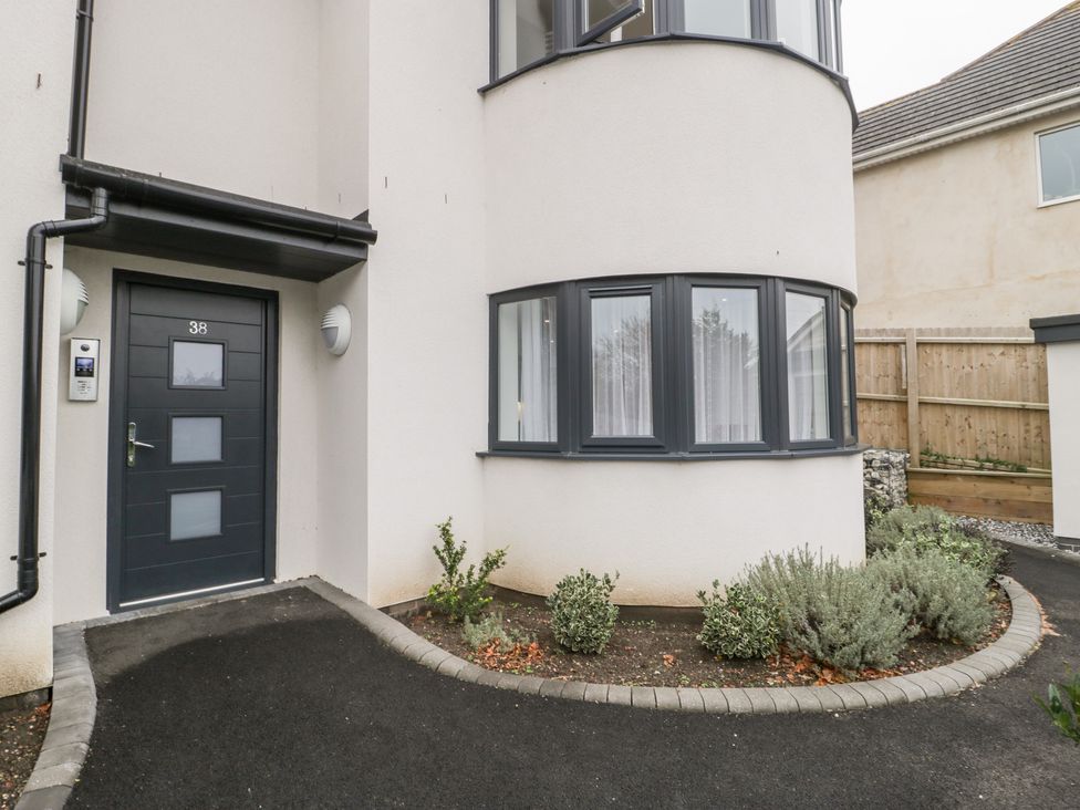 The front entrance of a building with a dark door numbered 38 and a curved window with plants along the path at Flat 2 38 Preston Road Weymouth