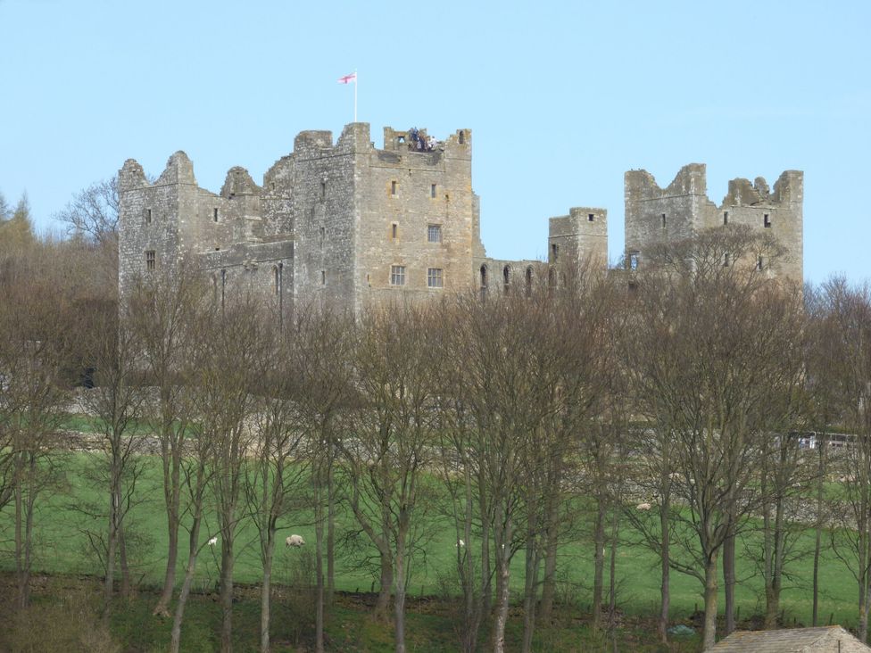 A stone castle on a hill behind trees with a flag flying at the top at Valley View in West Witton