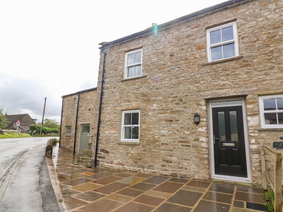 Stone exterior of a house with windows a black door and a wet paved walkway at White Lea in Reeth