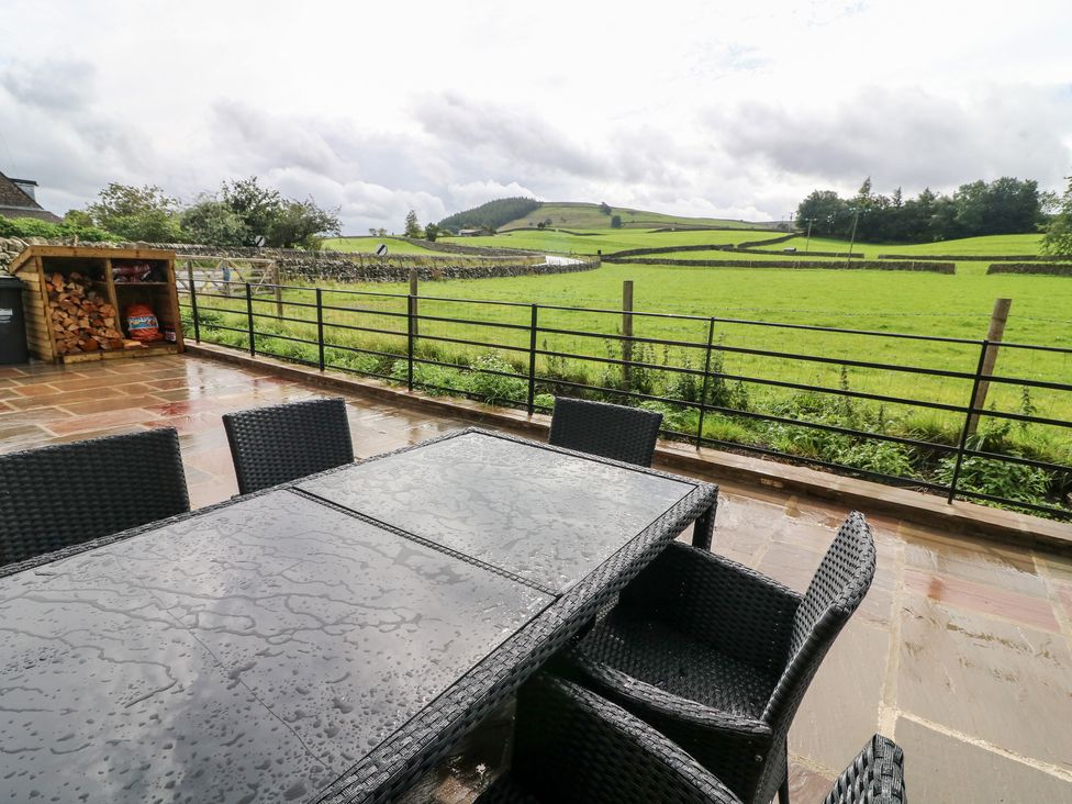 A wet outdoor patio with a table and chairs overlooking a green field with stone walls at White Lea in Reeth