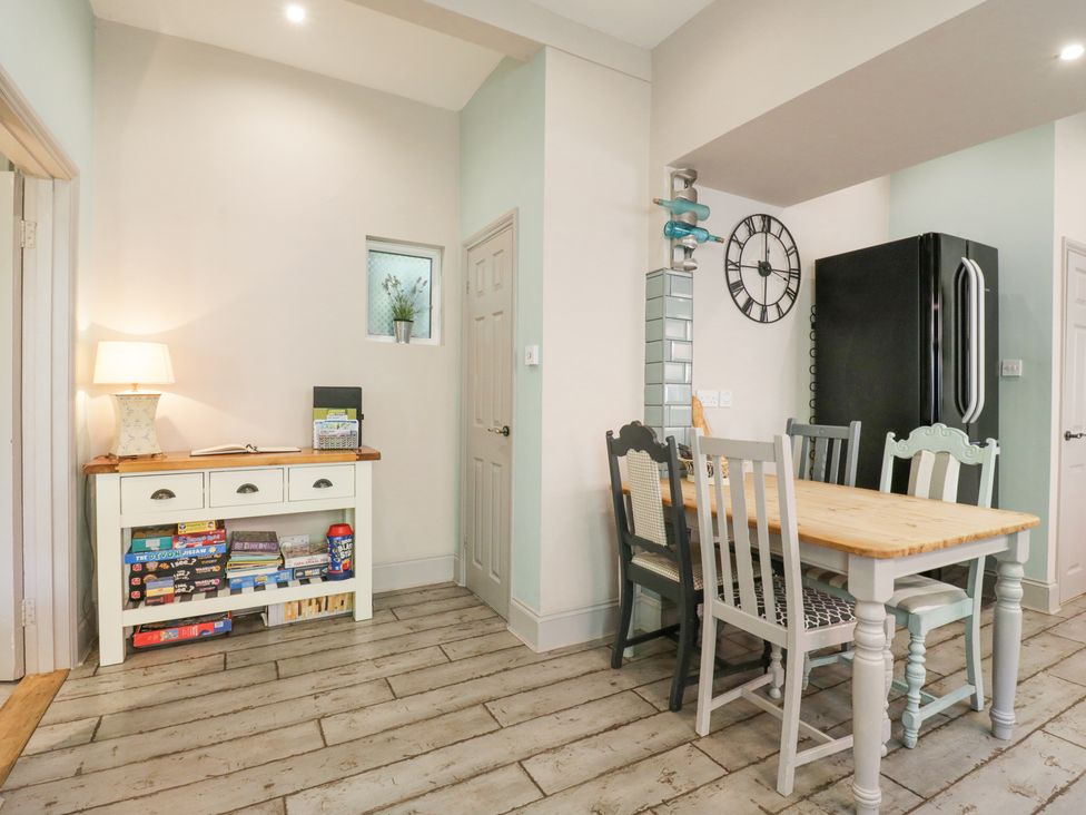 A dining area with a wooden table and mismatched chairs next to a black refrigerator and a side table with board games and a lamp at Saxon Lodge Cottage Felixstowe Suffolk