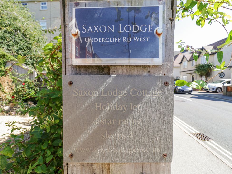 A wooden post with two signs indicating Saxon Lodge and Saxon Lodge Cottage on Undercliff Rd West in a residential street with houses and cars