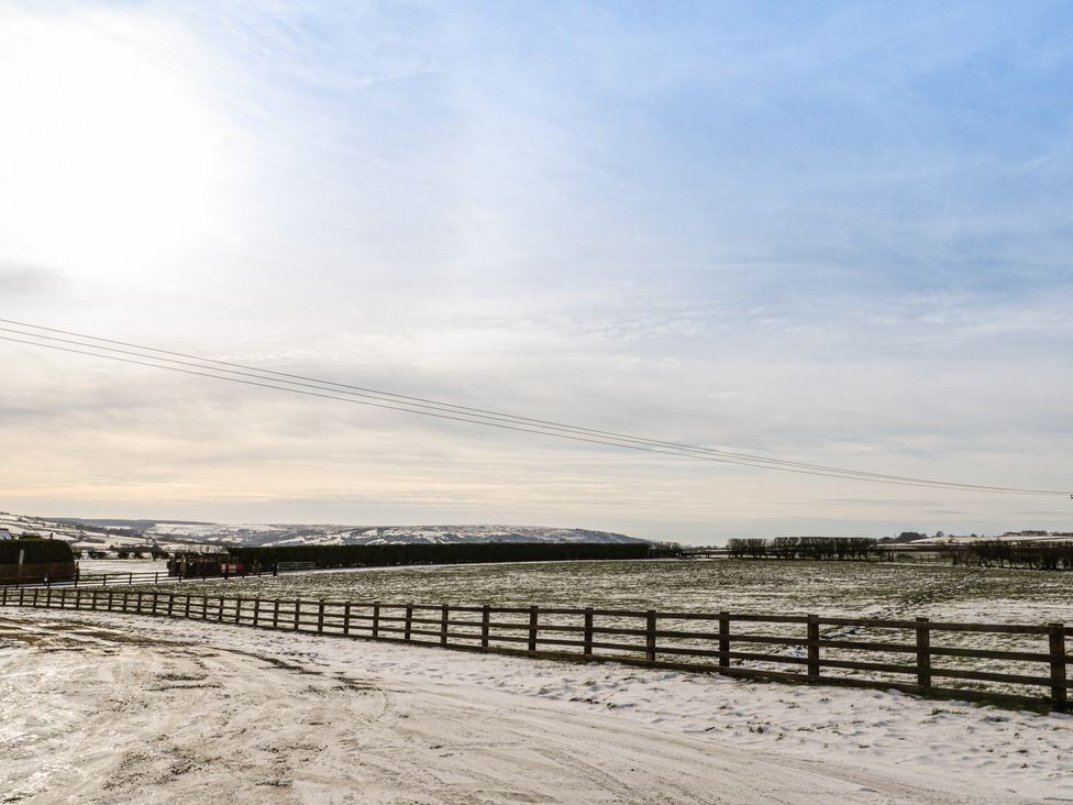 A fenced field with light snow cover and a partly cloudy sky at Cartwheel Cottage at Broadings Farm in Whitby