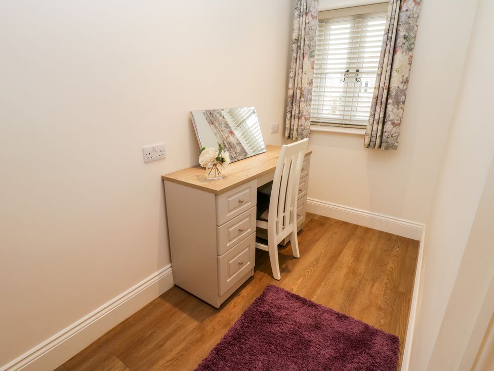 A small room with a wooden desk and white chair next to a window with floral curtains and a purple rug on the floor at Cartwheel Cottage at Broadings Farm in Whitby