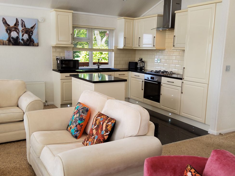A kitchen with cream cabinets and black countertops next to a living area with beige sofas and colorful cushions at Lodge 11 in Tavistock