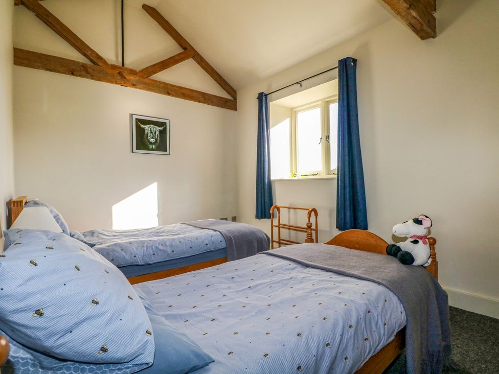 A bedroom with two single beds blue curtains and wooden beams at The Cowshed in Sedlescombe near Westfield