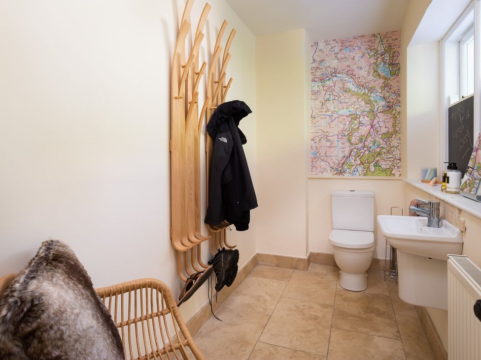A bathroom with a toilet sink coat rack and a chair with a fur cushion at Grass Ings in Langdale