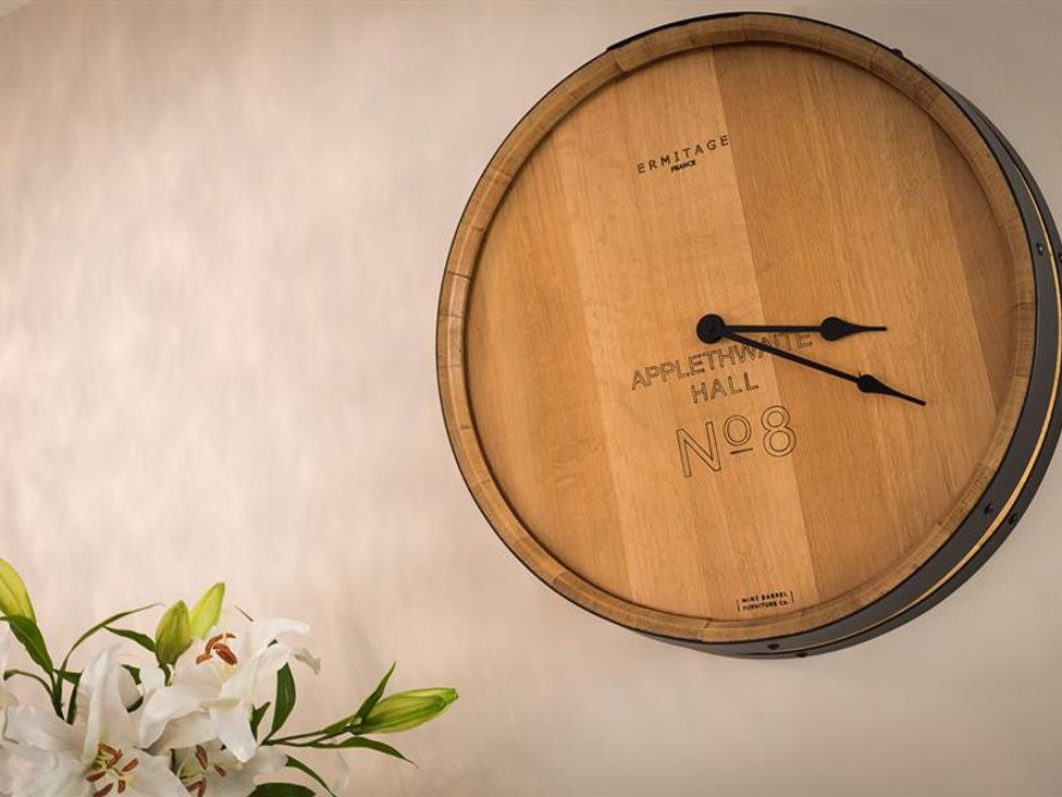 A wooden wall clock made from a barrel top with white flowers below at Appletwhite Hall No 8