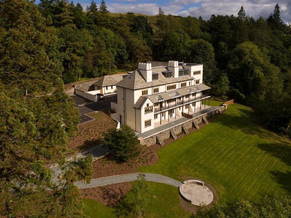 A large white multi-story house surrounded by trees and a grassy lawn with a stone pathway leading to a circular stone seating area at Hygge at No 8 in Windermere
