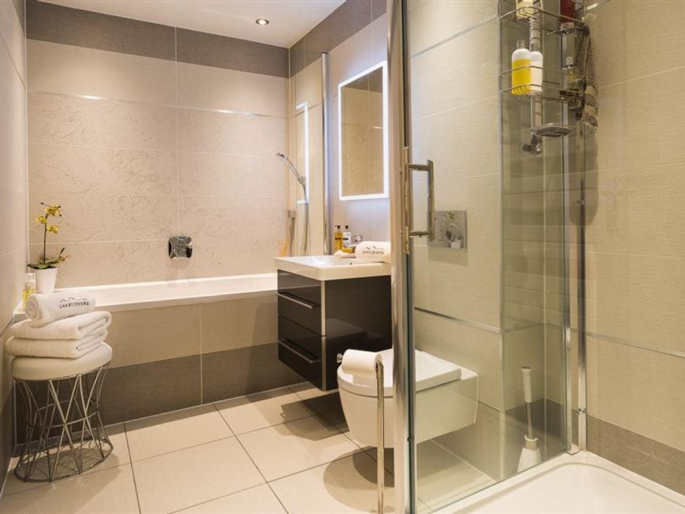 A bathroom with a bathtub a glass shower a wall-mounted sink a toilet and towels on a stool at Hygge at No 8 in Windermere
