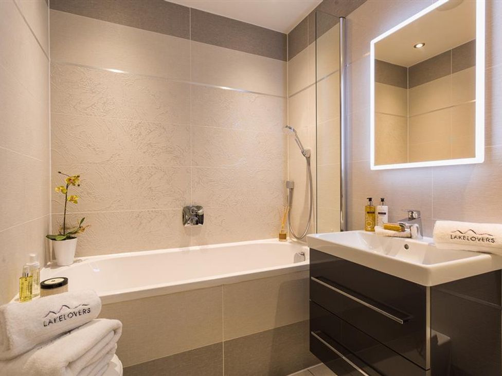 A bathroom with a bathtub a shower a sink with toiletries and a mirror at Hygge at No 8 in Windermere