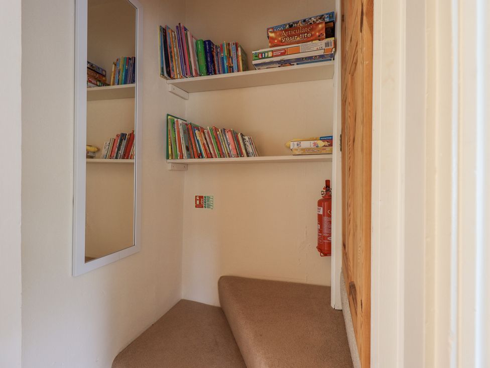 A small corner with carpeted stairs shelves with books and board games a wall mirror and a fire extinguisher at Ash Cottage in Windermere