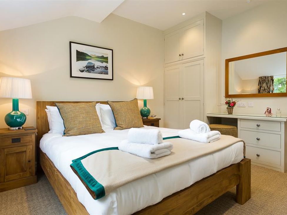 A bedroom with a wooden bed two bedside tables with lamps a dresser with a mirror and folded towels at Goody Raise in Grasmere
