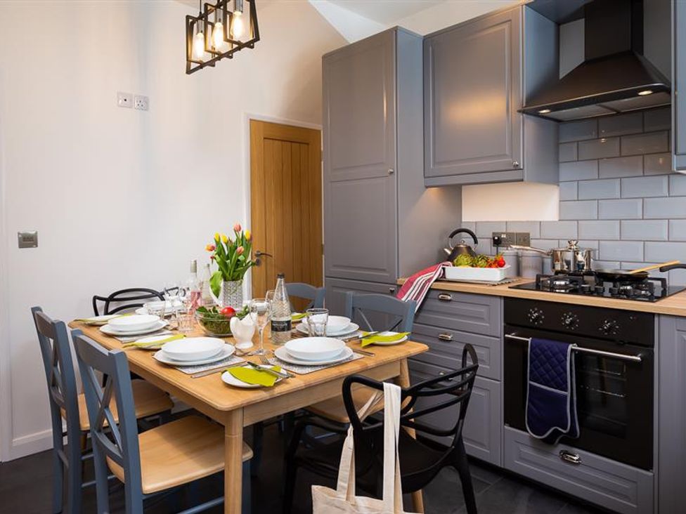 A kitchen with grey cabinets a wooden dining table set with plates glasses and a vase of flowers at Fell Cottage in Ambleside