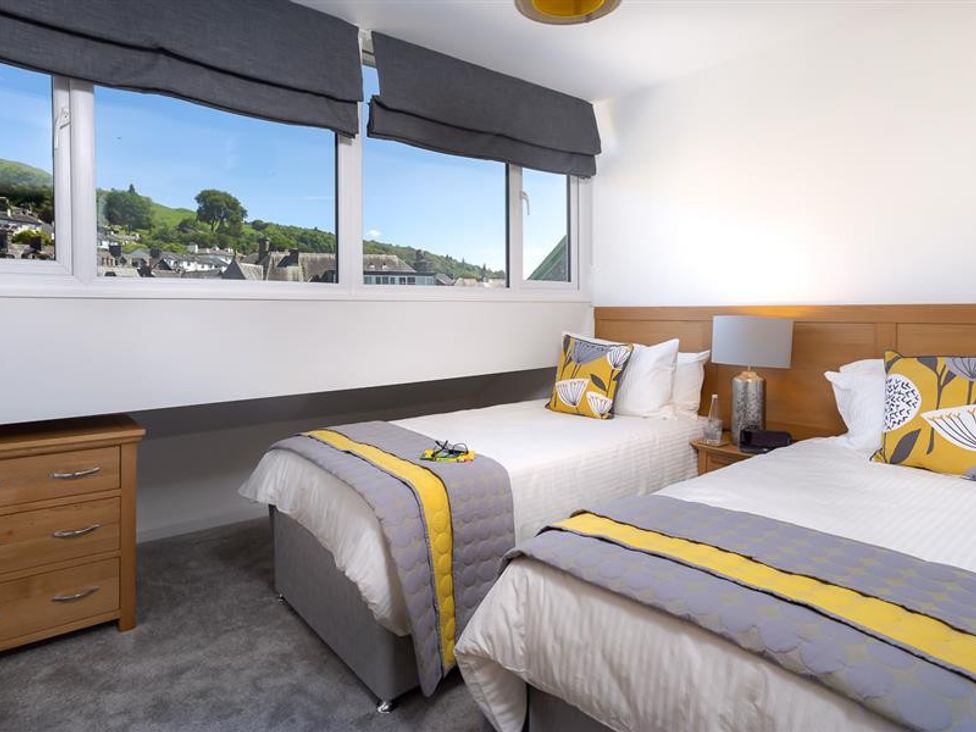A bedroom with two single beds beside a window with a view of houses and hills at Fell Cottage Ambleside