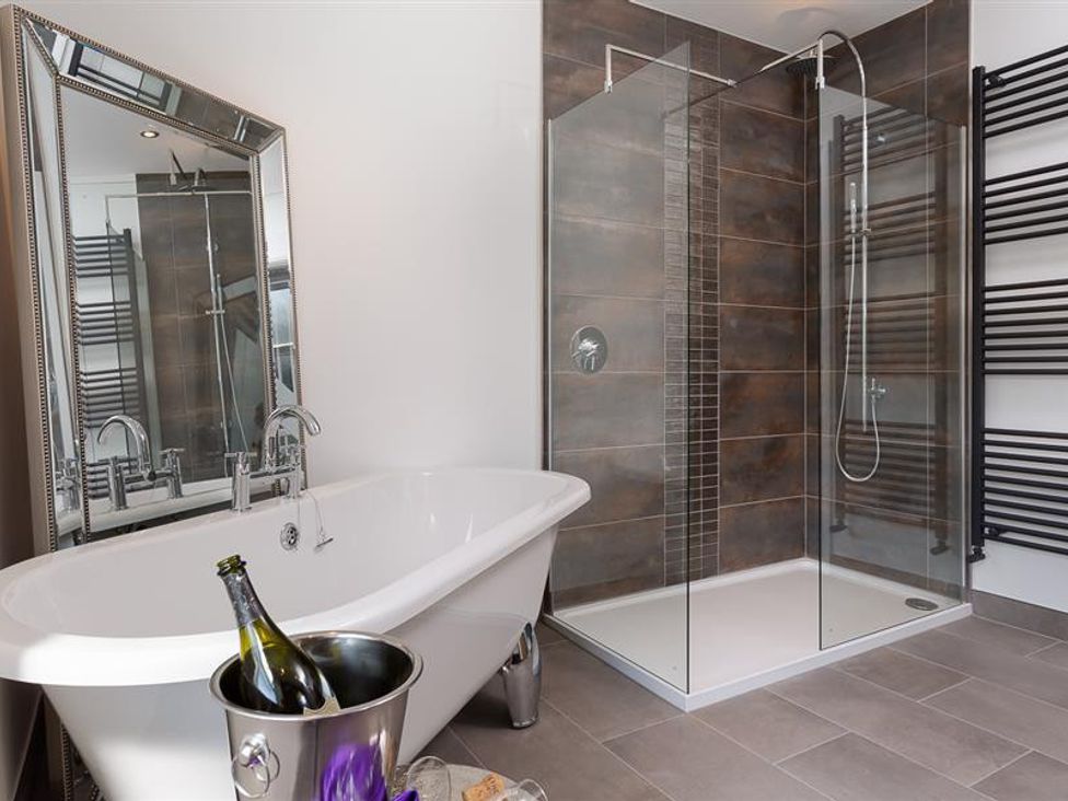 A bathroom with a freestanding bathtub a glass-walled shower and a large mirror at Fell Cottage in Ambleside