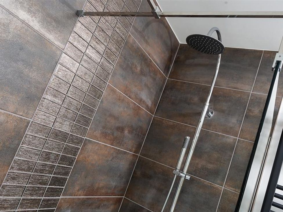 A shower area with brown and textured tiles and a chrome showerhead at Fell Cottage in Ambleside