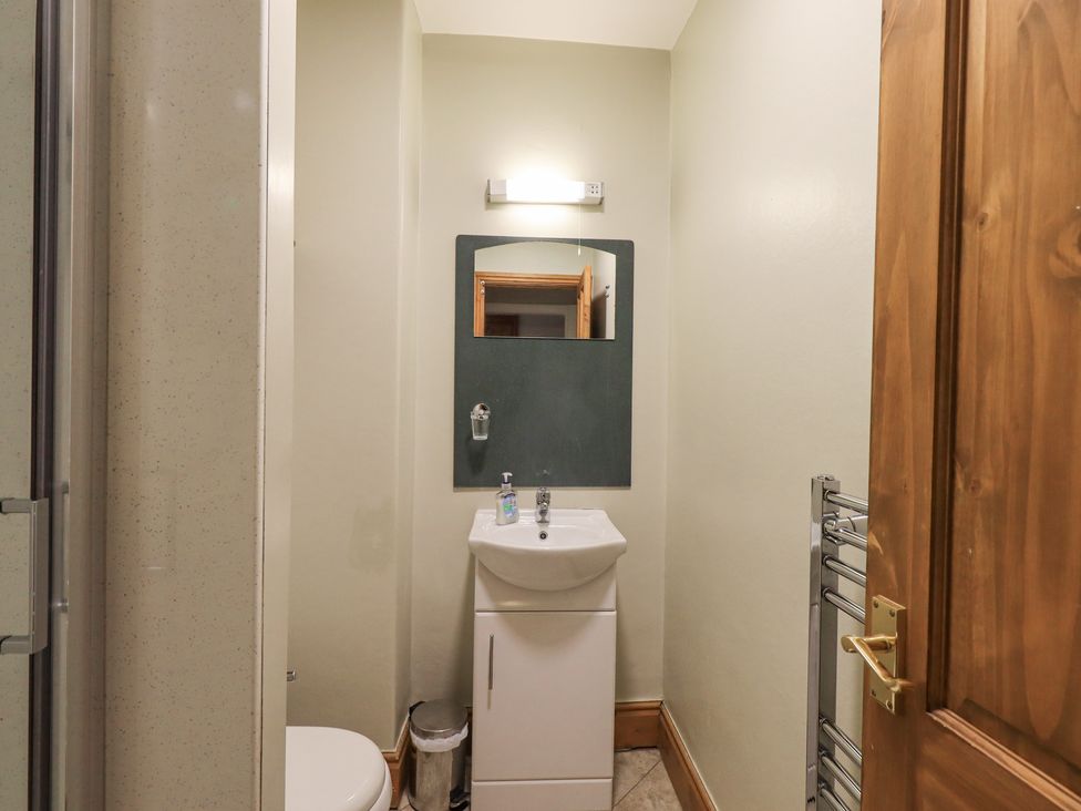 A small bathroom with a sink cabinet mirror trash bin towel rack and a wooden door at Millans Garth in Ambleside