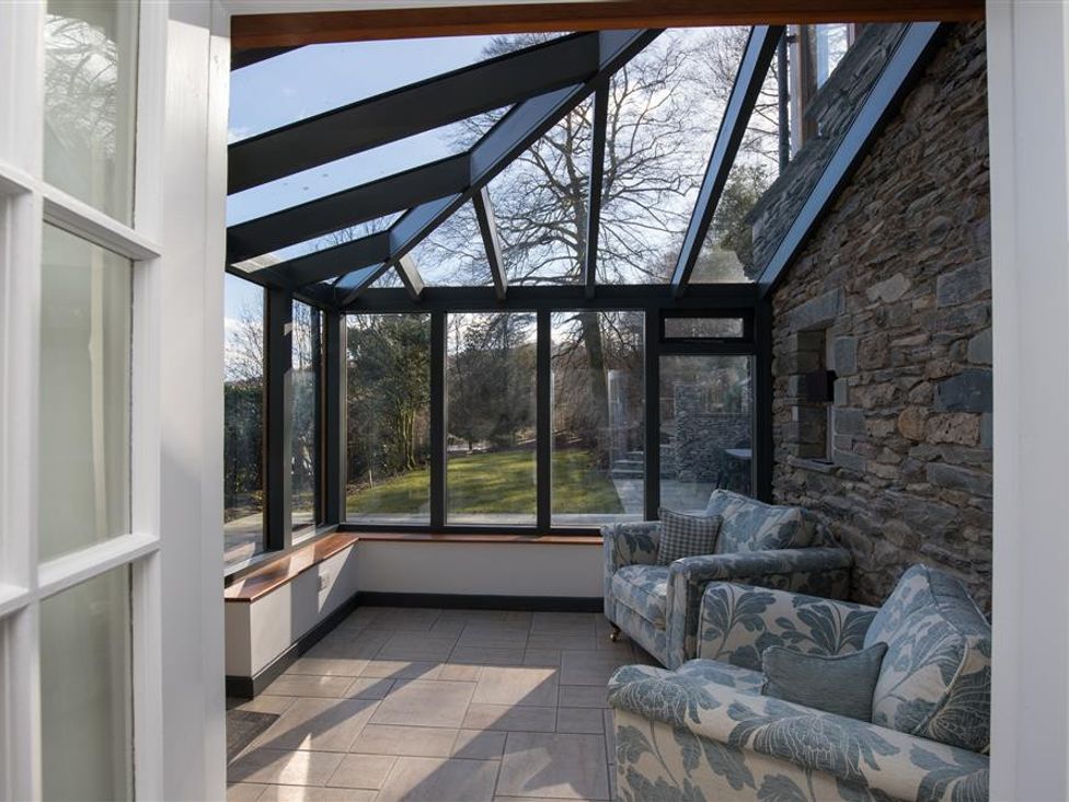 A sunroom with two armchairs and a stone wall at Spring Cottage in Loughrigg Fell