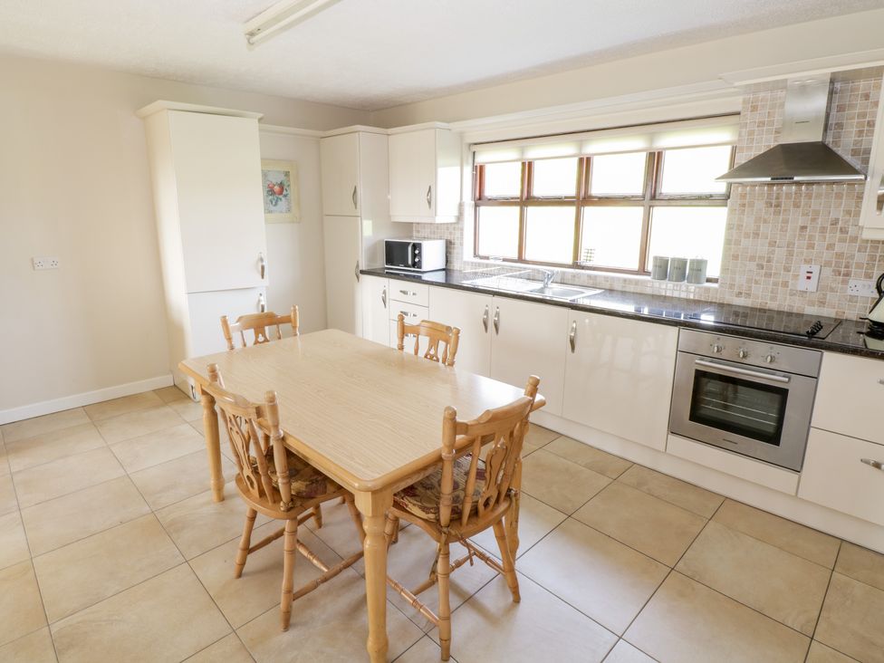 A kitchen with a wooden table and four chairs next to white cabinets and appliances at Brow O The Hill in Ballyshannon