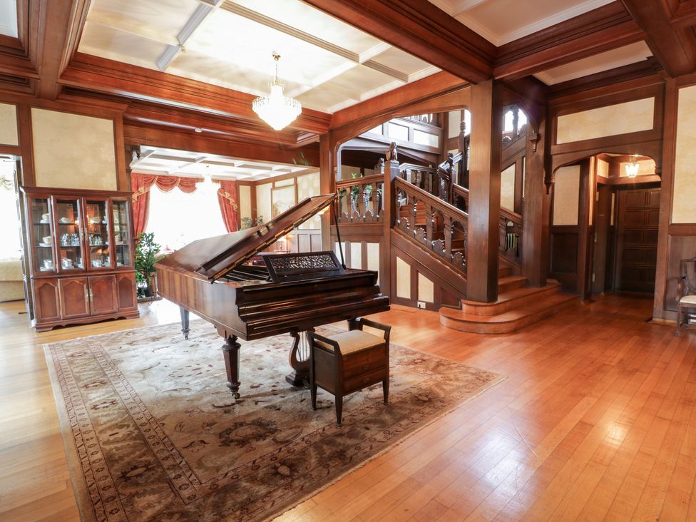 A room with a grand piano on a rug near wooden stairs and a glass cabinet at Auchentroig House Buchlyvie
