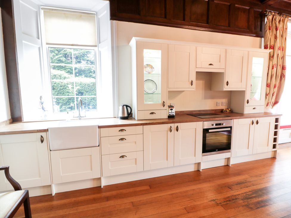 A kitchen with white cabinets a wooden countertop a sink under a large window and an oven at Auchentroig House Buchlyvie