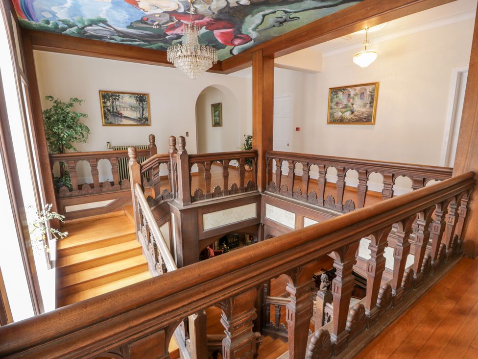 A wooden staircase with ornate railings paintings on the walls and a colorful ceiling mural at Auchentroig House in Buchlyvie
