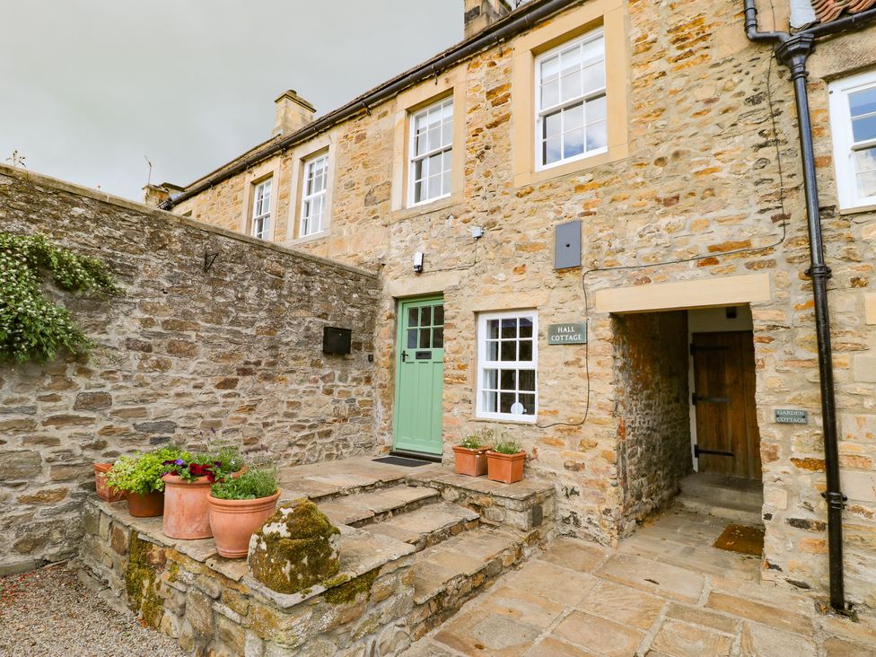 Stone exterior of a cottage with a green door and potted plants at Hall Cottage in Ovington