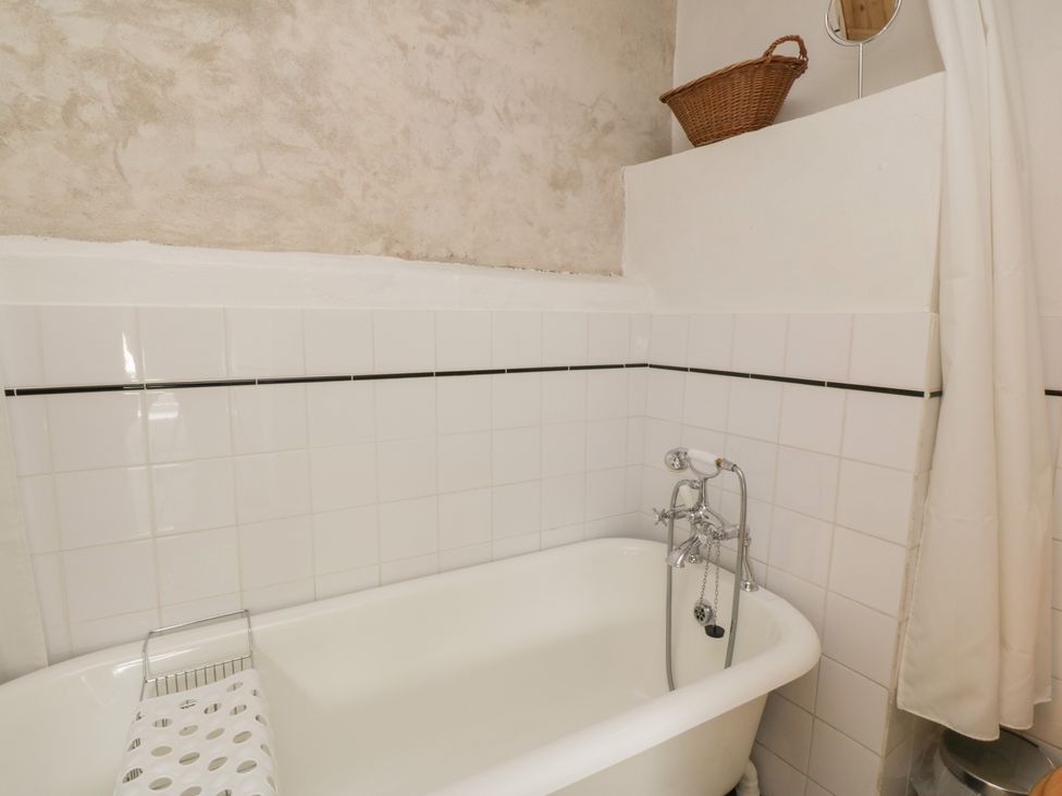 A bathroom with a white bathtub a shower curtain a basket and white tiled walls at The Pend in Whithorn