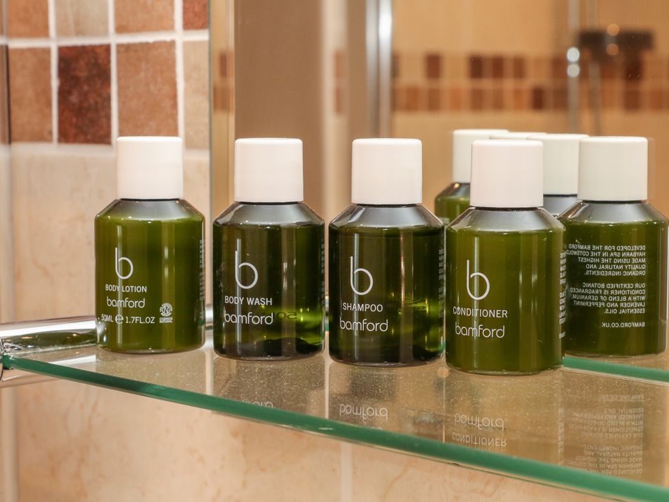 Green bottles of body lotion body wash shampoo and conditioner on a glass shelf in a bathroom at Brookhouse in Castleton Peak District