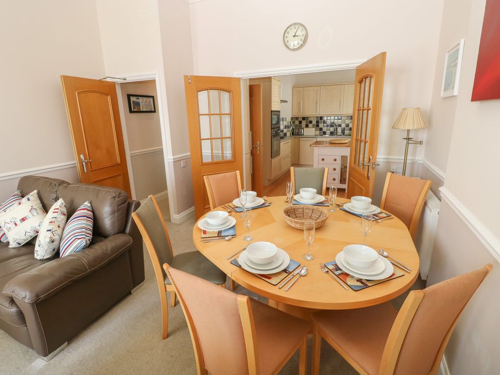 A dining room with a round wooden table set for six and a brown leather sofa at 6 South Beach Court in Tenby