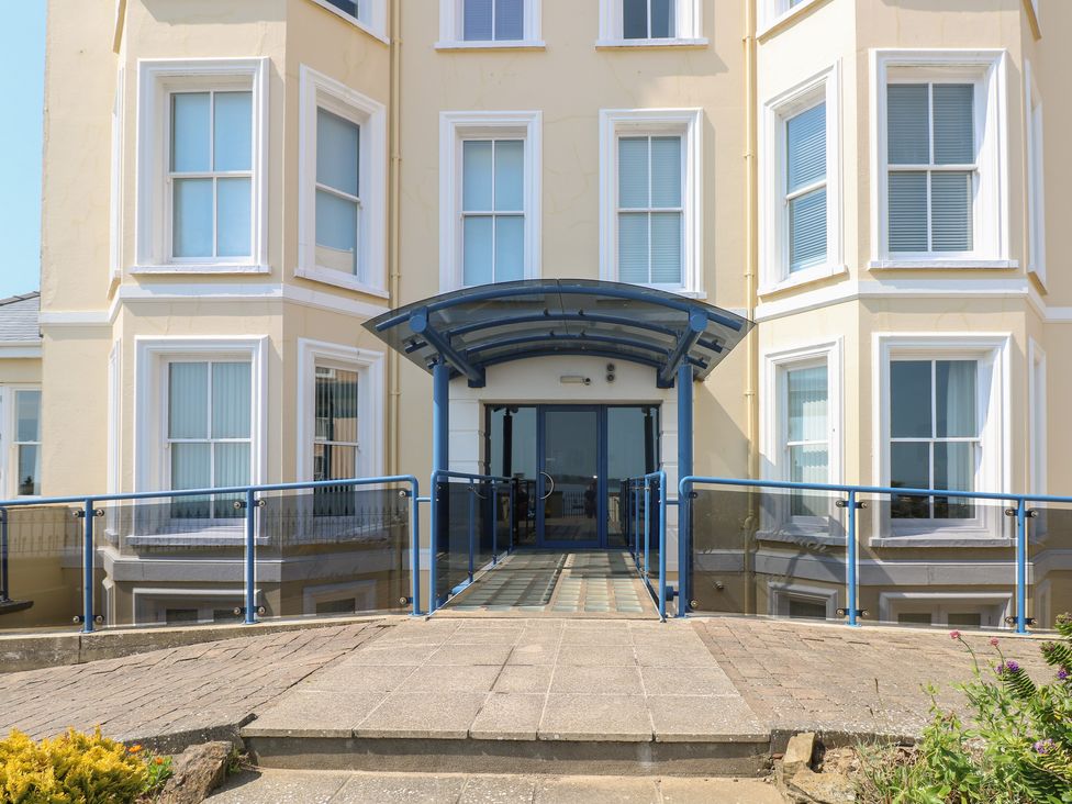 The entrance ramp with blue railings leading to a glass door of a beige building with multiple windows at 6 South Beach Court Tenby
