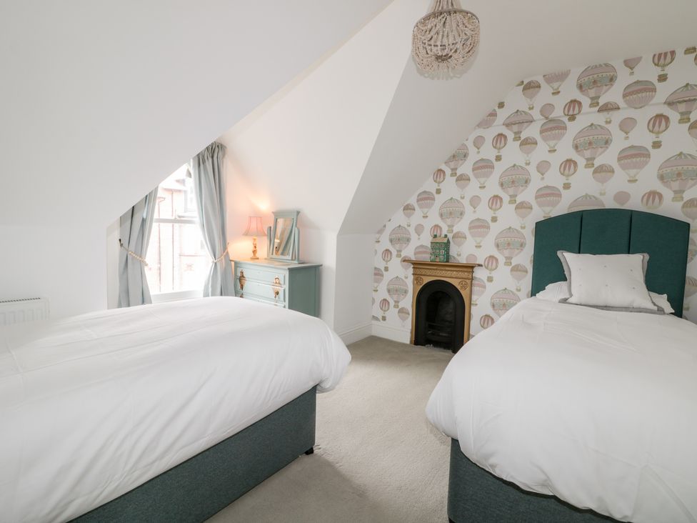 A bedroom with two single beds white bedding a small fireplace a dresser with a lamp and mirror and a window with curtains at 39 West Street Scarborough