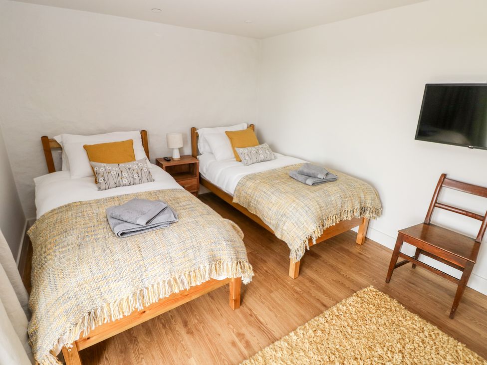 A bedroom with two single beds a bedside table with lamp a wooden chair and a wall-mounted TV at Glowty Brynbedw in Efailwen