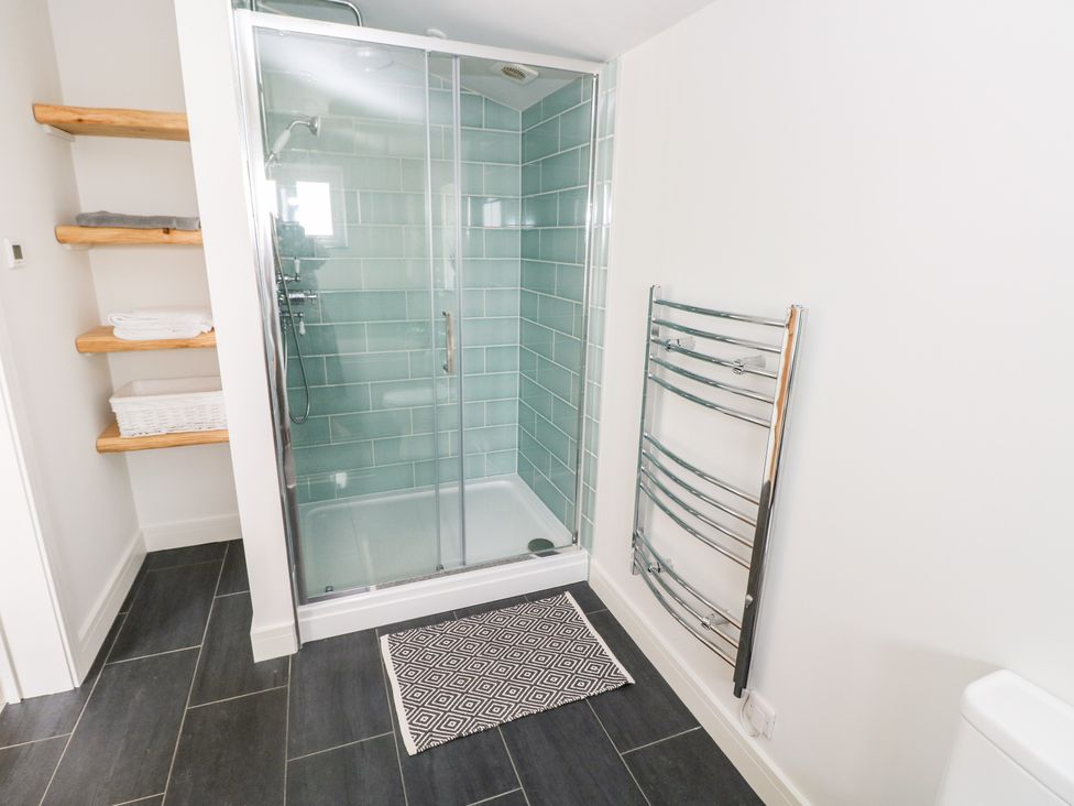 A bathroom with a glass shower enclosure tiled with green tiles shelves with towels and a chrome towel radiator at Glowty Brynbedw in Efailwen