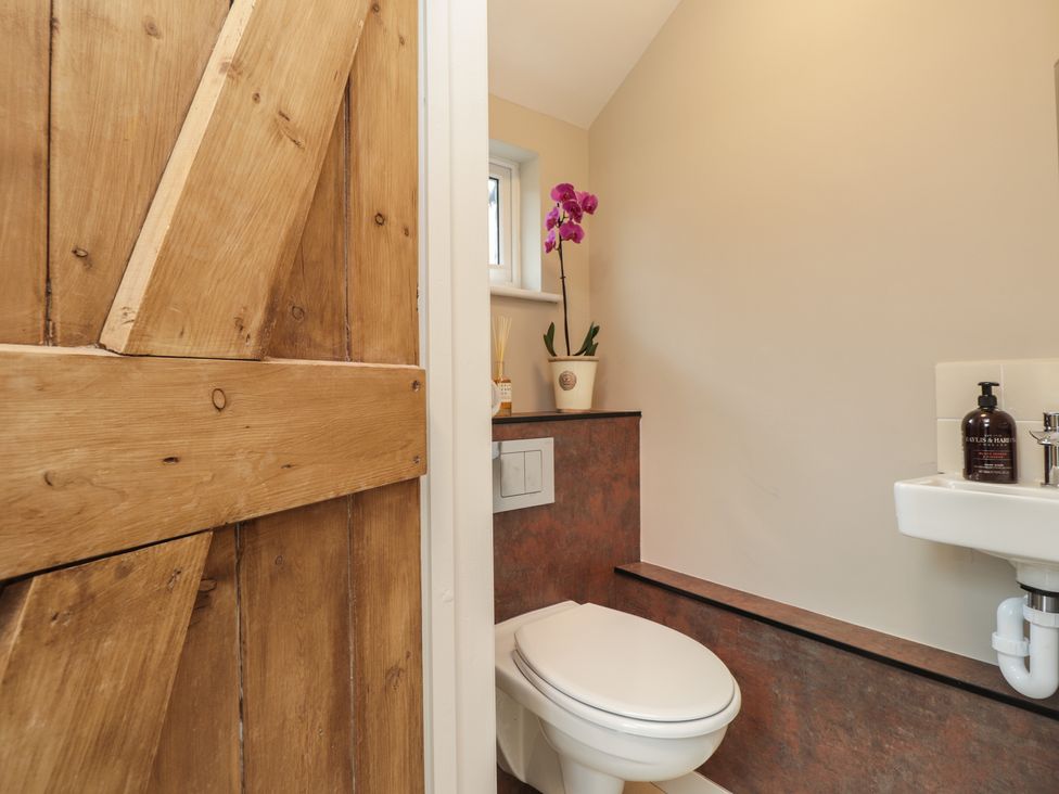 A bathroom with a wooden door a toilet a small sink and a purple orchid plant at Vine Cottage in Tenterden