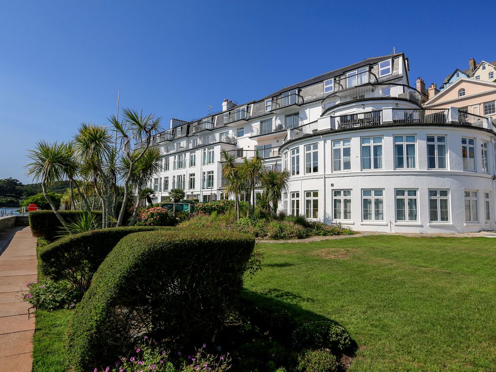 White multi-story building with balconies surrounded by trimmed hedges palm trees and grass at 34 The Salcombe in Salcombe