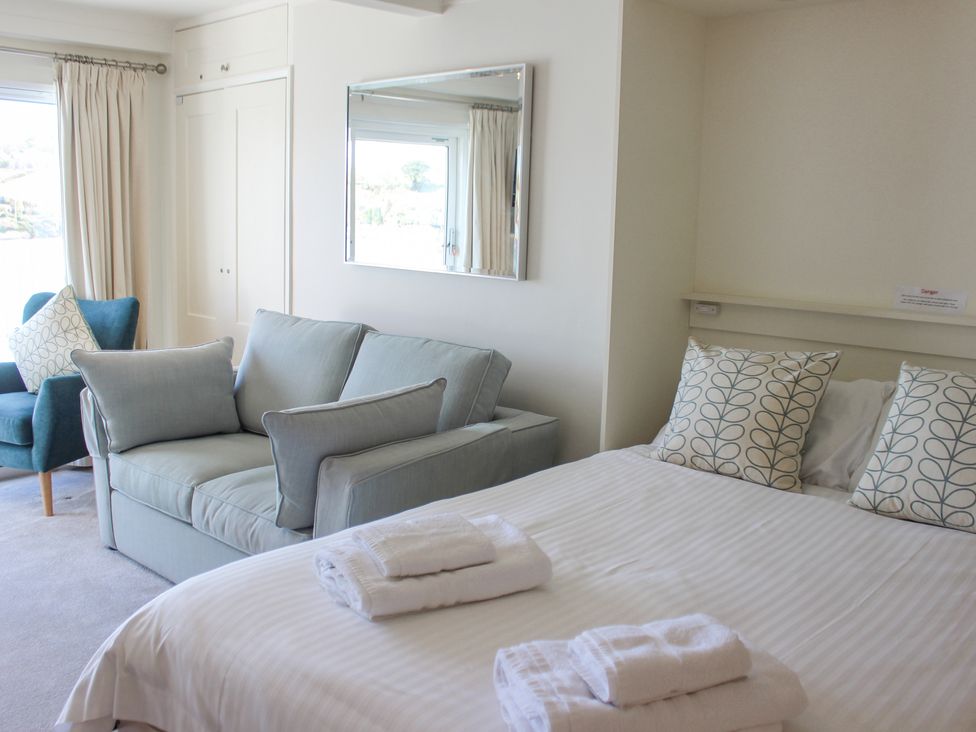 A bedroom with a bed with folded towels on it a sofa with cushions and an armchair near a window at 34 The Salcombe in Salcombe